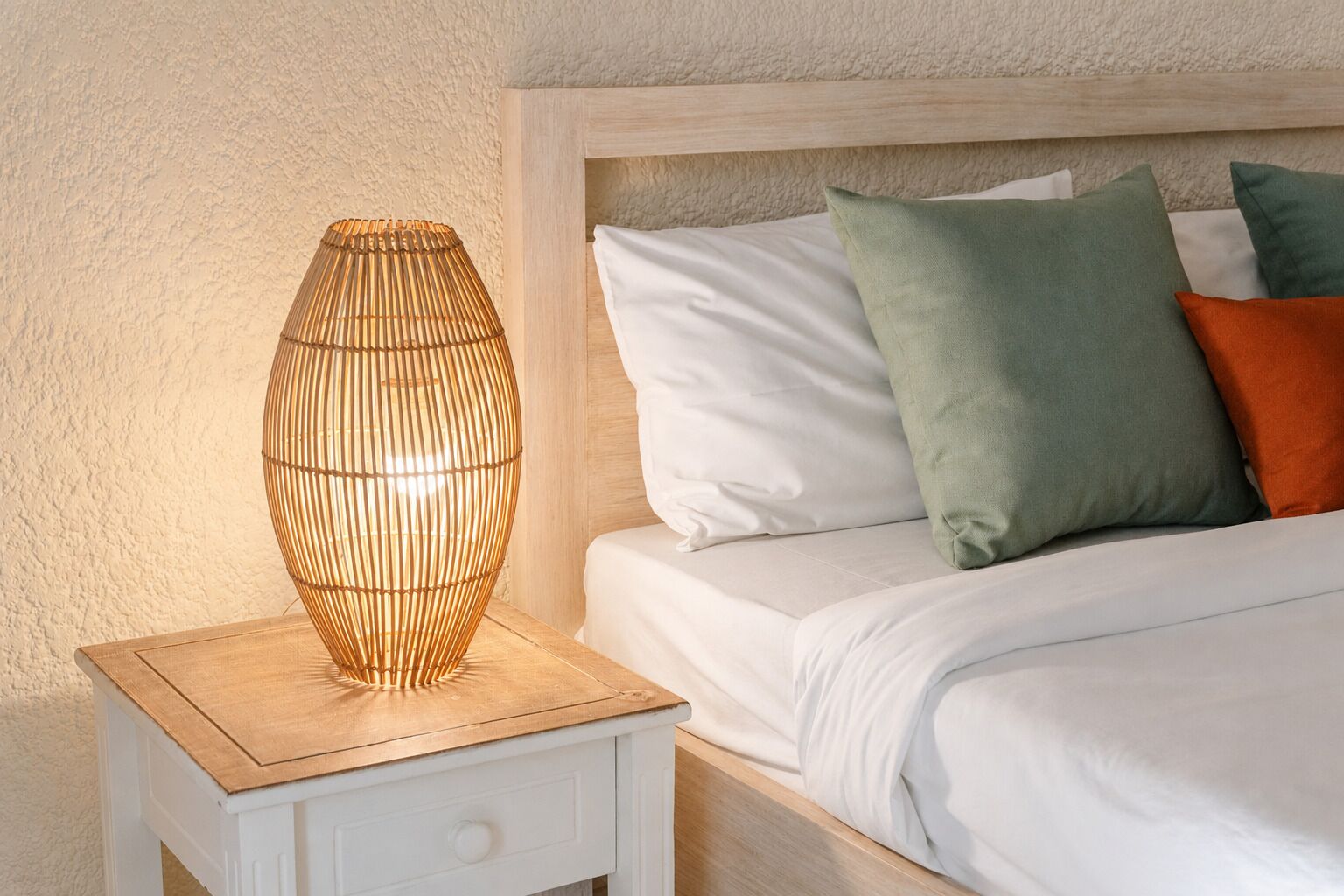 A bed with white bedding and multiple pillows, a bedside table with a lamp, and a textured wall.