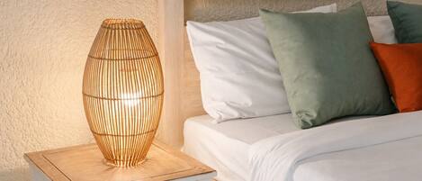 A bed with white bedding and multiple pillows, a bedside table with a lamp, and a textured wall.