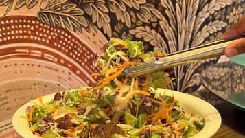 Un tazón de ensalada con una variedad de vegetales y zanahoria rallada, sostenido con pinzas.
