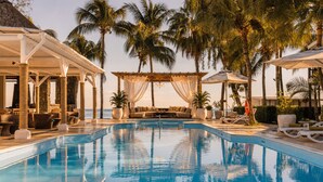 Un área de piscina con sillones reclinables, un espacio de descanso y palmeras.
