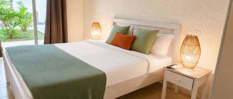 A hotel room with a bed, nightstands, a lamp, and a view of greenery outside.