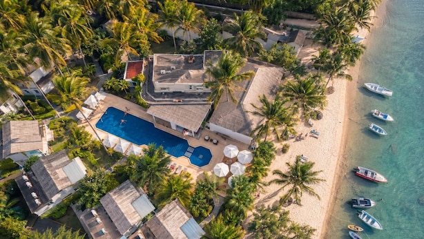 Vista aérea de un complejo turístico con piscina, playa y barcos.