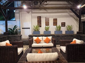 An outdoor seating area with wicker furniture and cushions, potted plants, and a stone wall.
