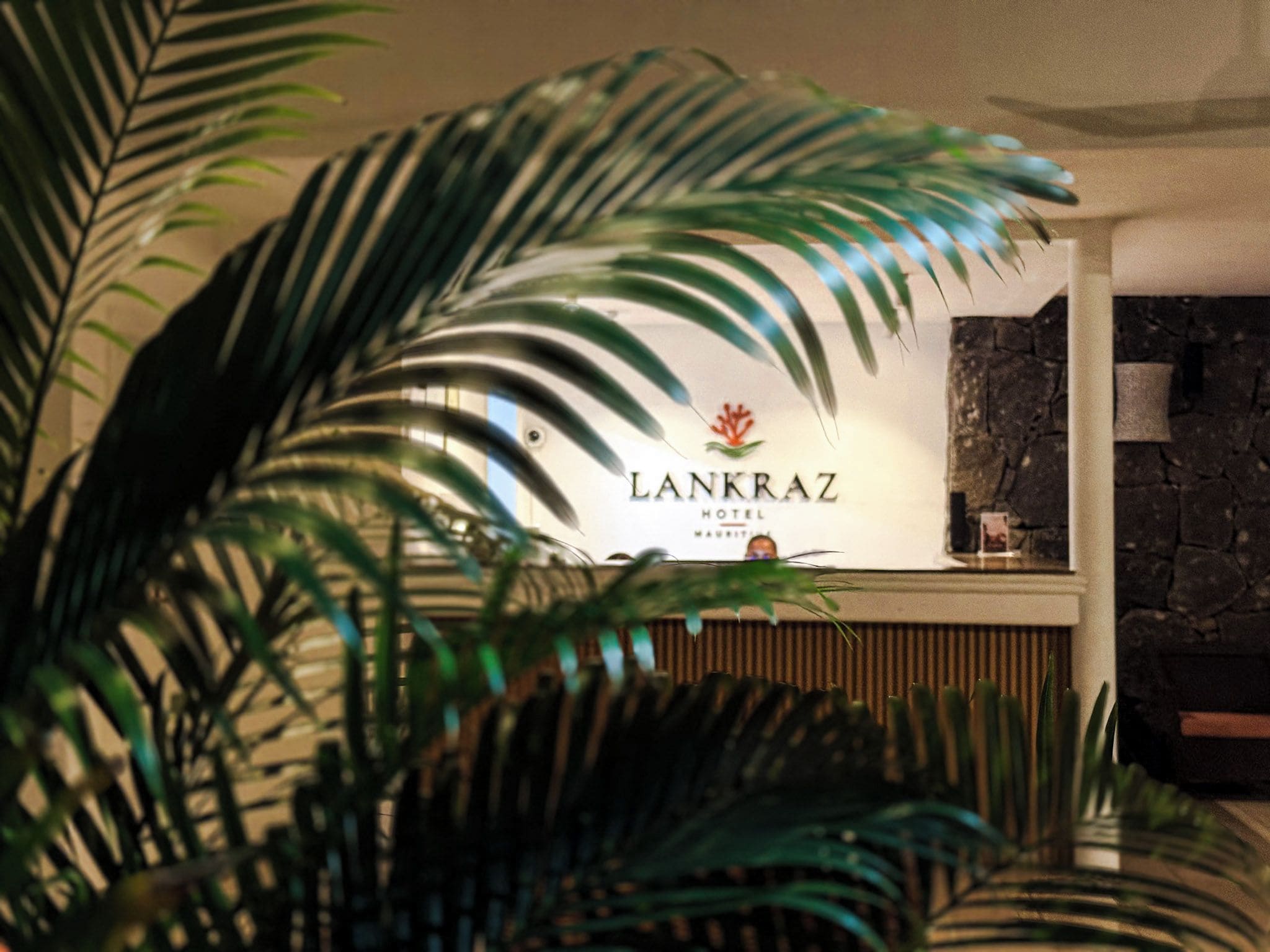 A reception desk with a sign for 'Lankraz Hotel Mauritius' and a stone wall in the background.