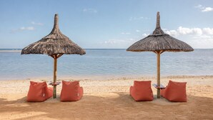 Dos sombrillas de paja en la playa, con cojines, con vistas a aguas tranquilas.