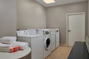 Un espacio para lavandería con toallas apiladas, una caja de detergente Tide y una lavadora y secadora Whirlpool.