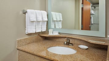 Un baño con encimera de granito, lavamanos y espejo.