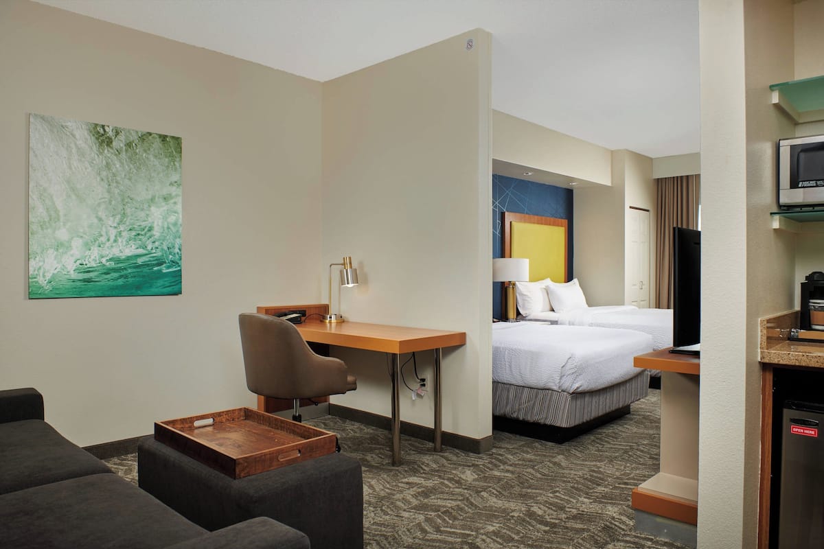 A hotel room with a bed, a desk, a chair, a TV, and a microwave.