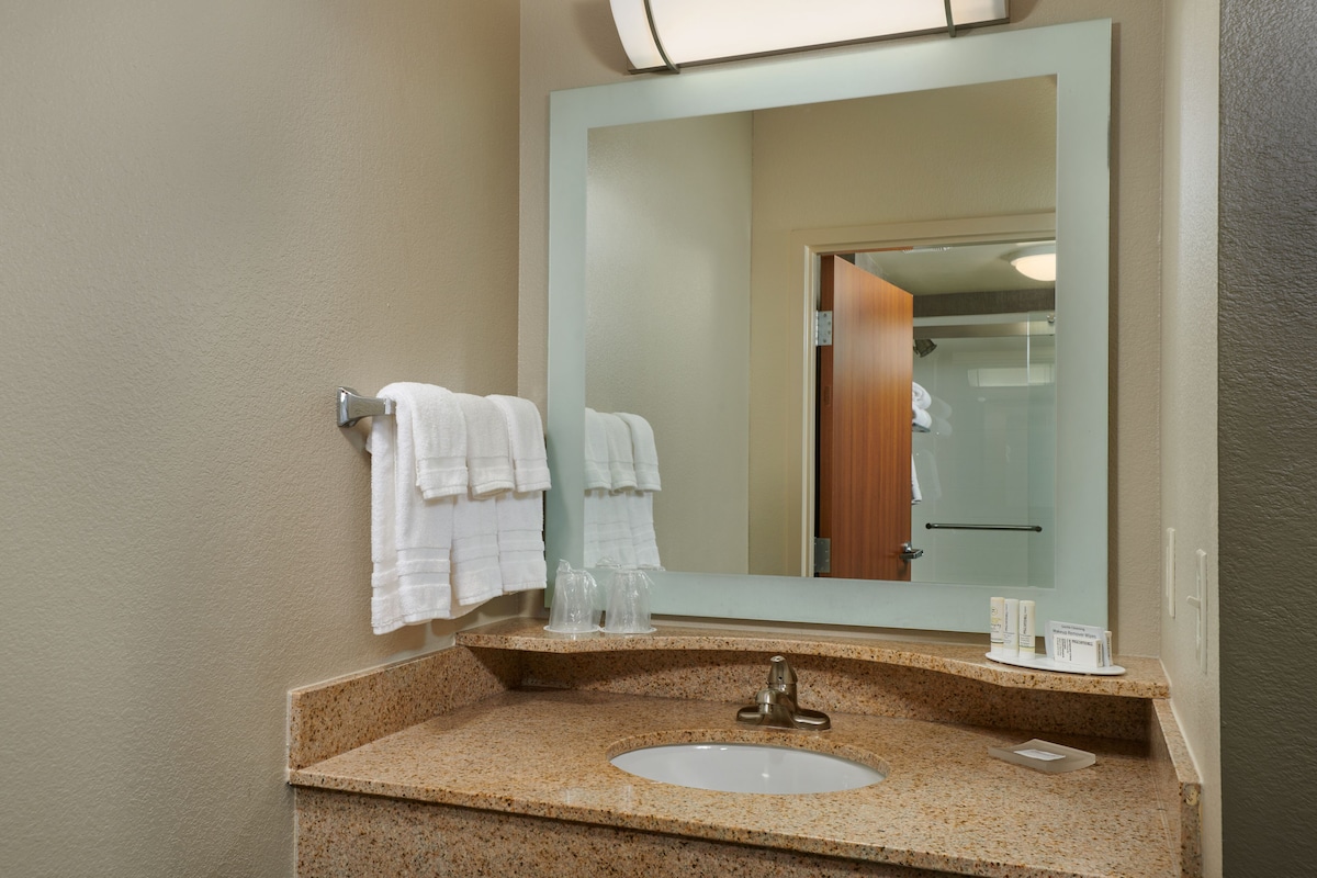 A bathroom with a granite countertop, a sink, a mirror, and two white towels hanging on a towel rack.