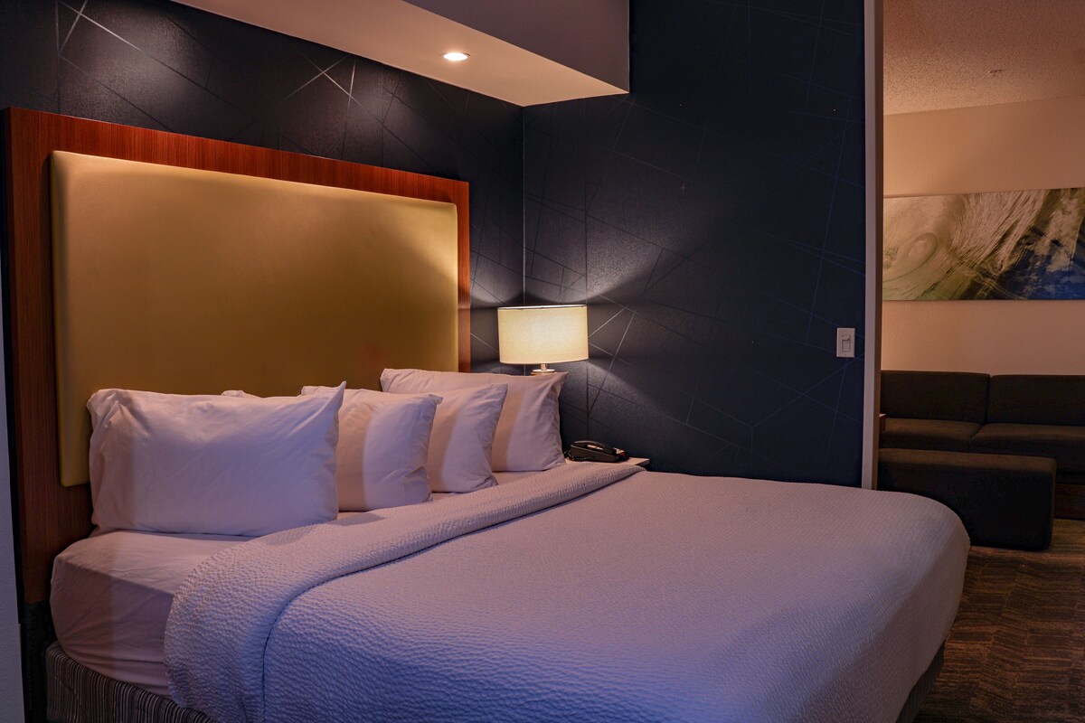 A hotel room with a large bed, a bedside lamp, and a couch.