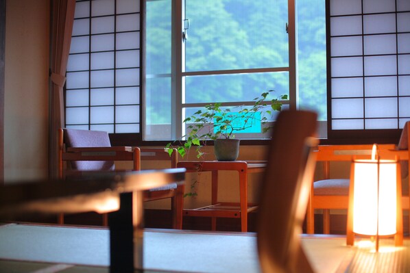 Una habitación tradicional japonesa con suelo de tatami, una mesa baja, una silla y una ventana con paneles shoji.