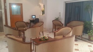 A lobby with four wooden armchairs, a small table with flowers, a desk with a computer, and a potted plant. - Ariha Hotel (Tunis)