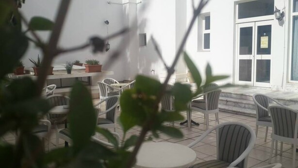 An outdoor seating area with white chairs and tables, potted plants, and a white building with large windows and a door. - Ariha Hotel (Tunis)