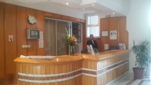 A reception desk with a wooden finish, a clock on the wall, and a potted plant. - Ariha Hotel (Tunis)