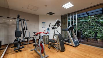 Un gimnasio con equipo de ejercicio diverso, ventanas amplias y vistas a zonas verdes.
