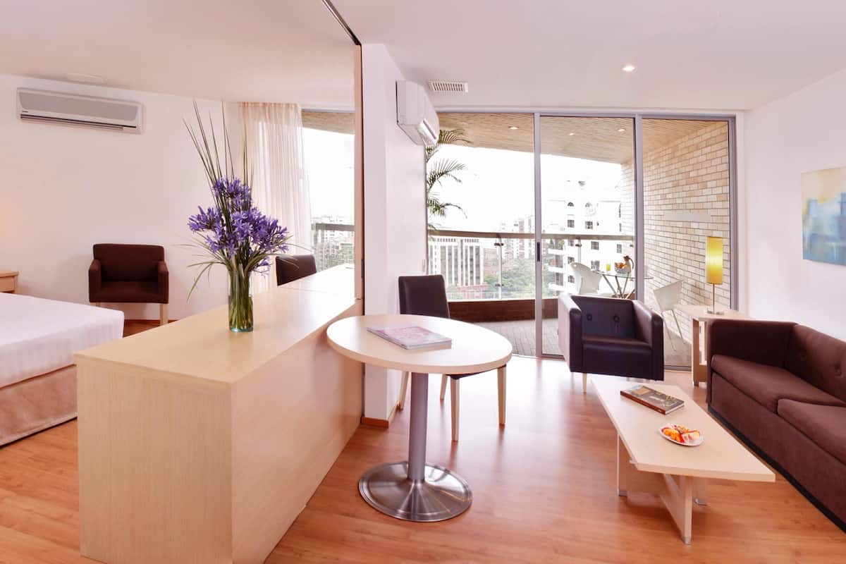 A hotel room with a bed, a desk, a sofa, and a balcony with a city view.