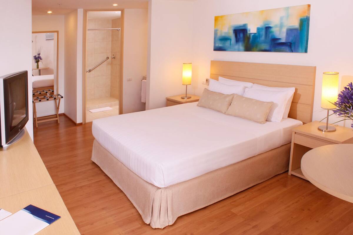 Ein Hotelzimmer mit einem großen Bett, Nachttischlampen, einem Fernseher und einem Gemälde an der Wand.