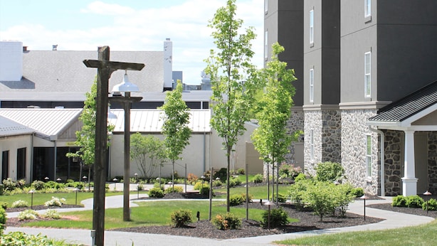 A courtyard with a stone building, a wooden pergola, and various trees. - AmishView Inn and Suites (Ronks)