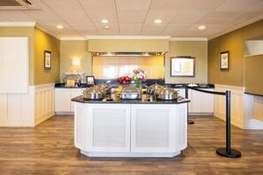 A buffet setup with covered food stations, a flower arrangement, and a white counter with a black base.