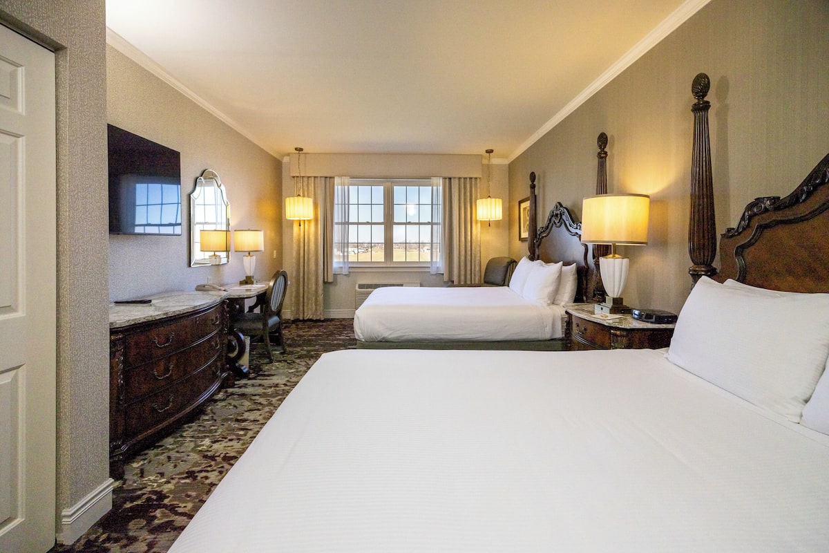 A hotel room with two beds, a dresser, a mirror, and a window with curtains.