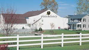 A white building with "plain & fancy" signage, surrounded by a white fence and a grassy area. - AmishView Inn and Suites (Ronks)