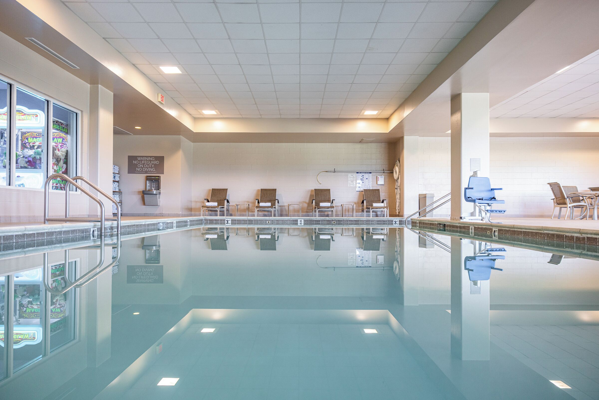 A swimming pool with a tiled floor, a changing room with benches, and a wall with a warning sign.