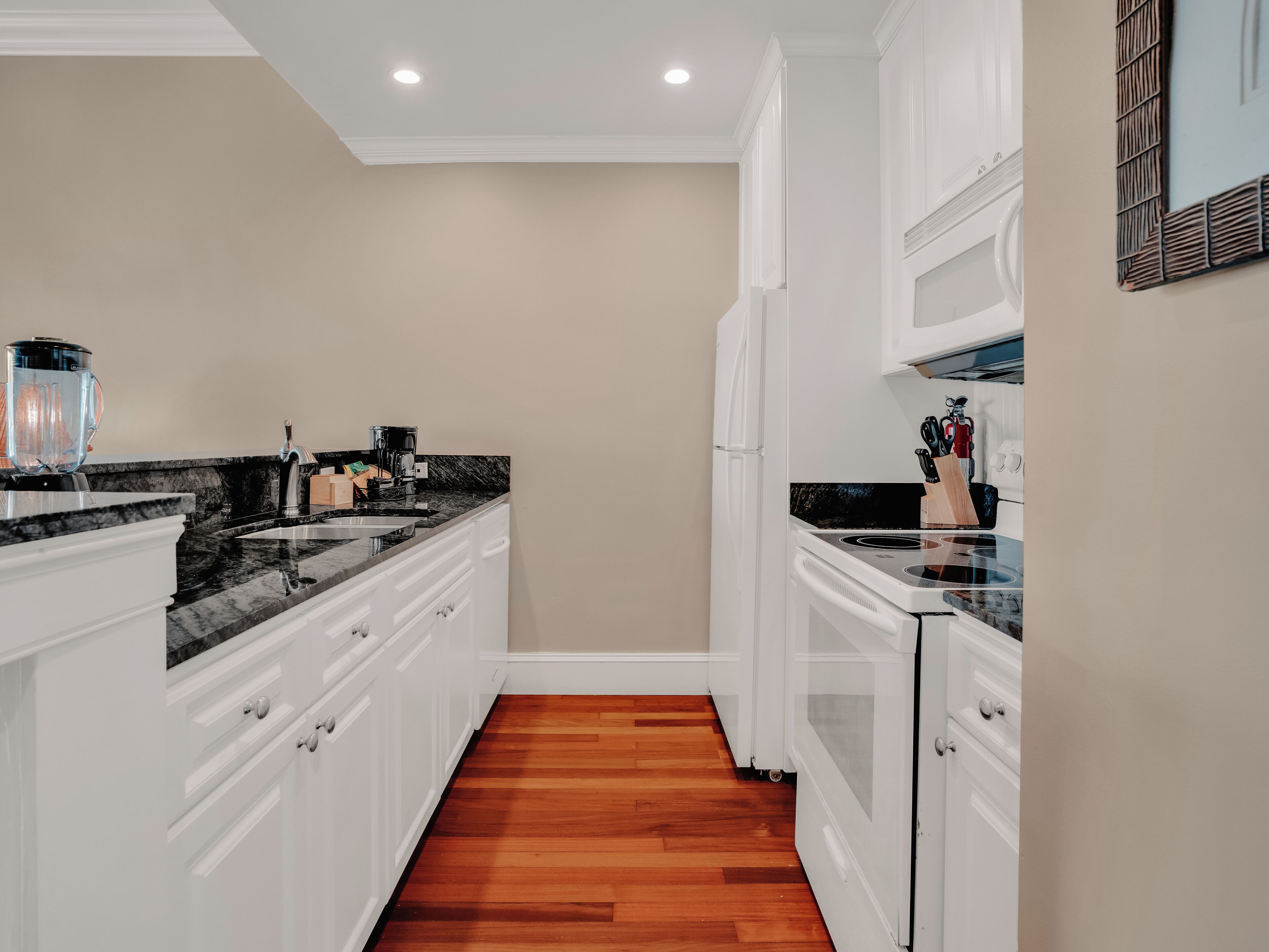 Una cocina moderna con armarios blancos, encimera de granito negro y suelo de madera.