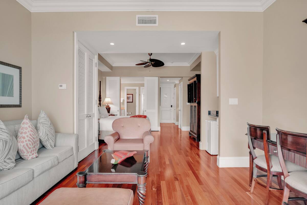 A spacious living room with a sofa, a coffee table, and a chair. There is a hallway leading to a bedroom.