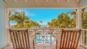 A wooden deck with two wooden chairs and a small table, overlooking a pool and palm trees. - Valentines Resort & Marina (Dunmore Town)