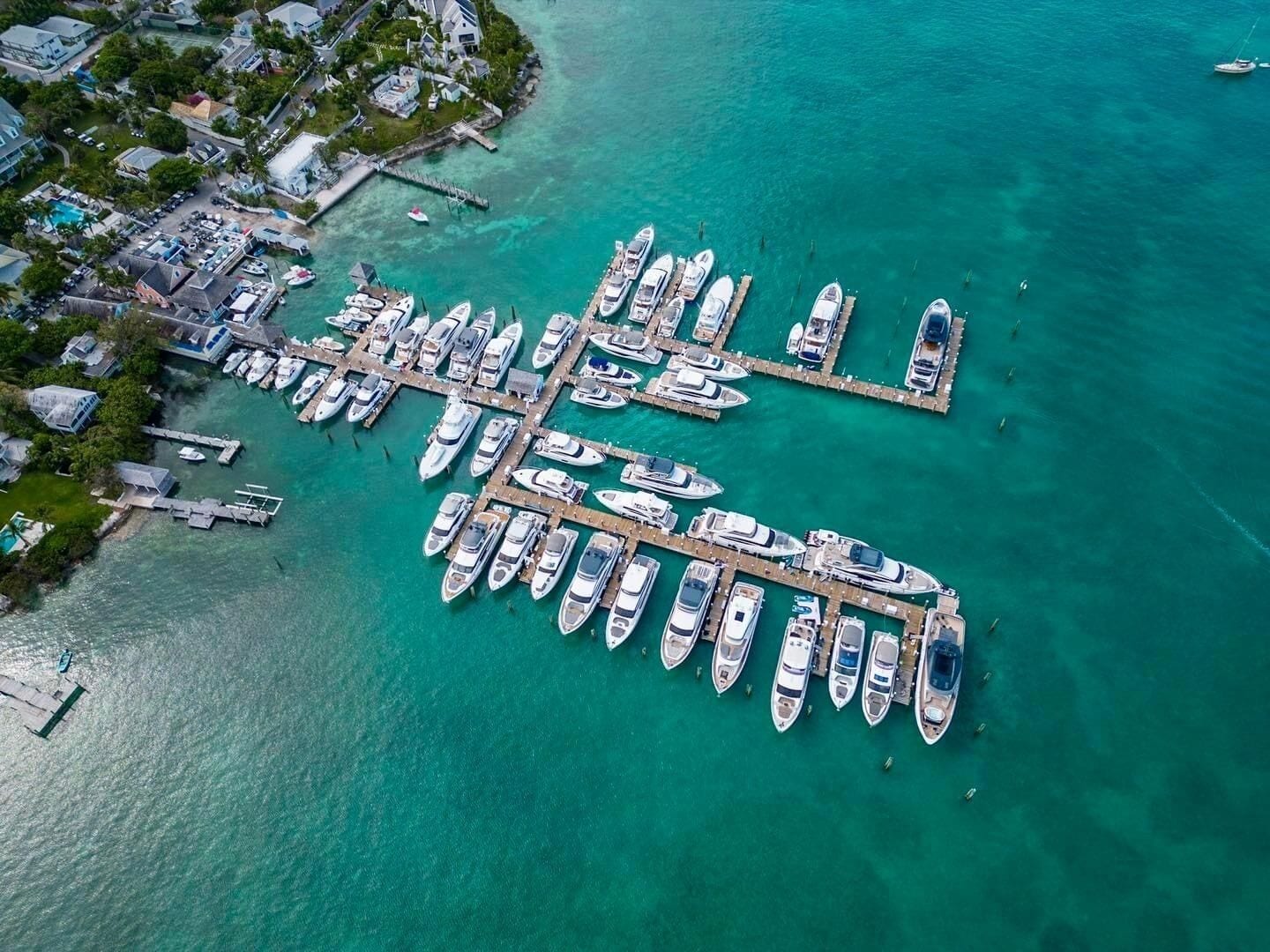Eine Luftaufnahme einer Marina mit zahlreichen vertäuten Booten, die durch Stege verbunden sind, und einer Wohngegend am Wasser.