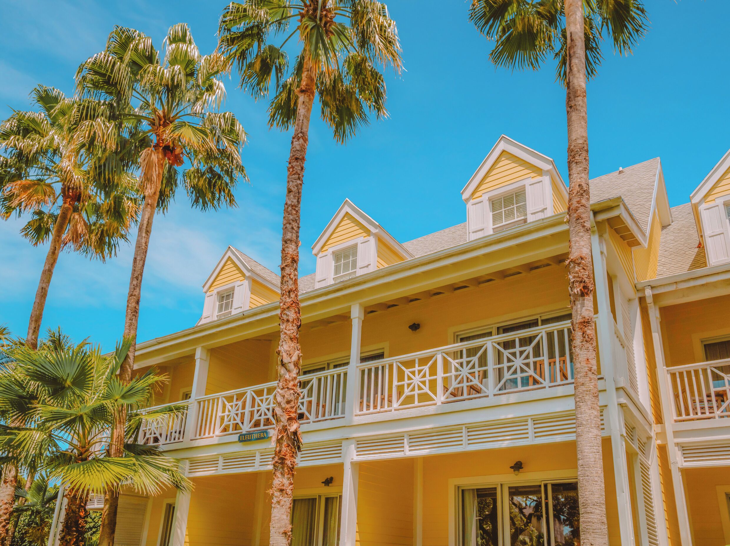 Un hotel de varios pisos con balcones, palmeras y un cielo azul despejado.