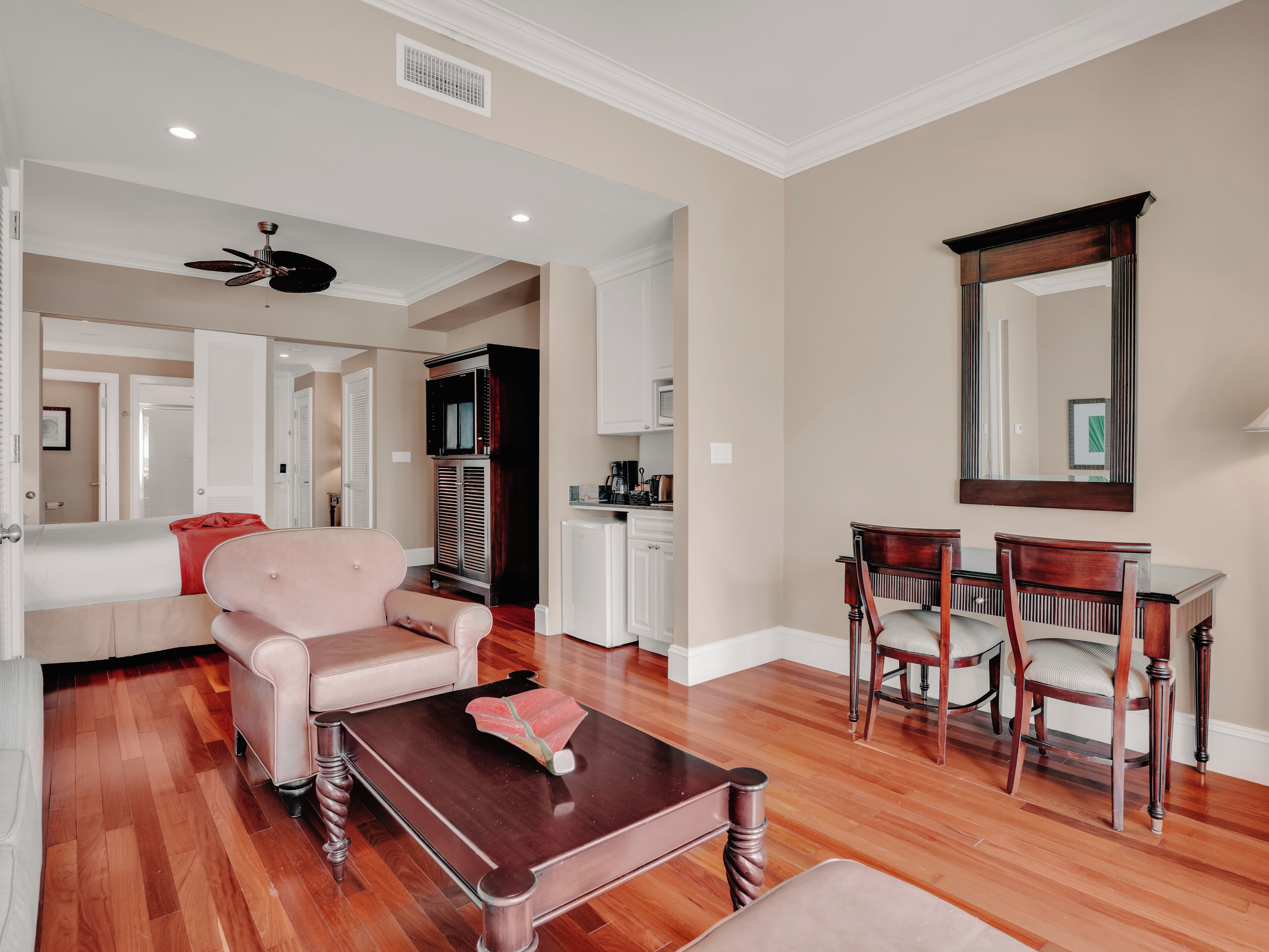 A spacious living room with a wooden coffee table, a pink sofa, and a dining area with wooden chairs and a large mirror.