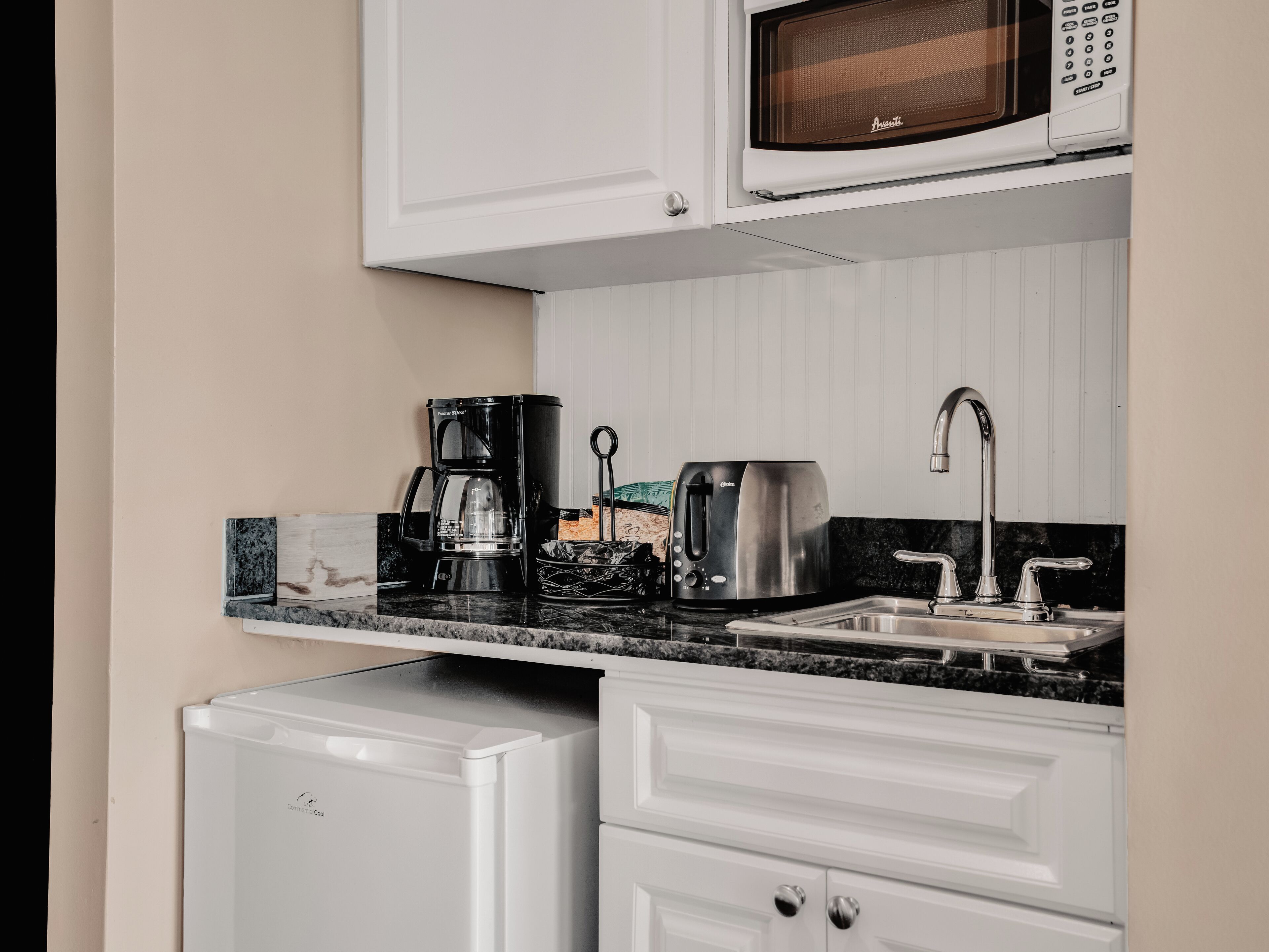 A compact kitchenette with a microwave, coffee maker, toaster, and a small refrigerator.