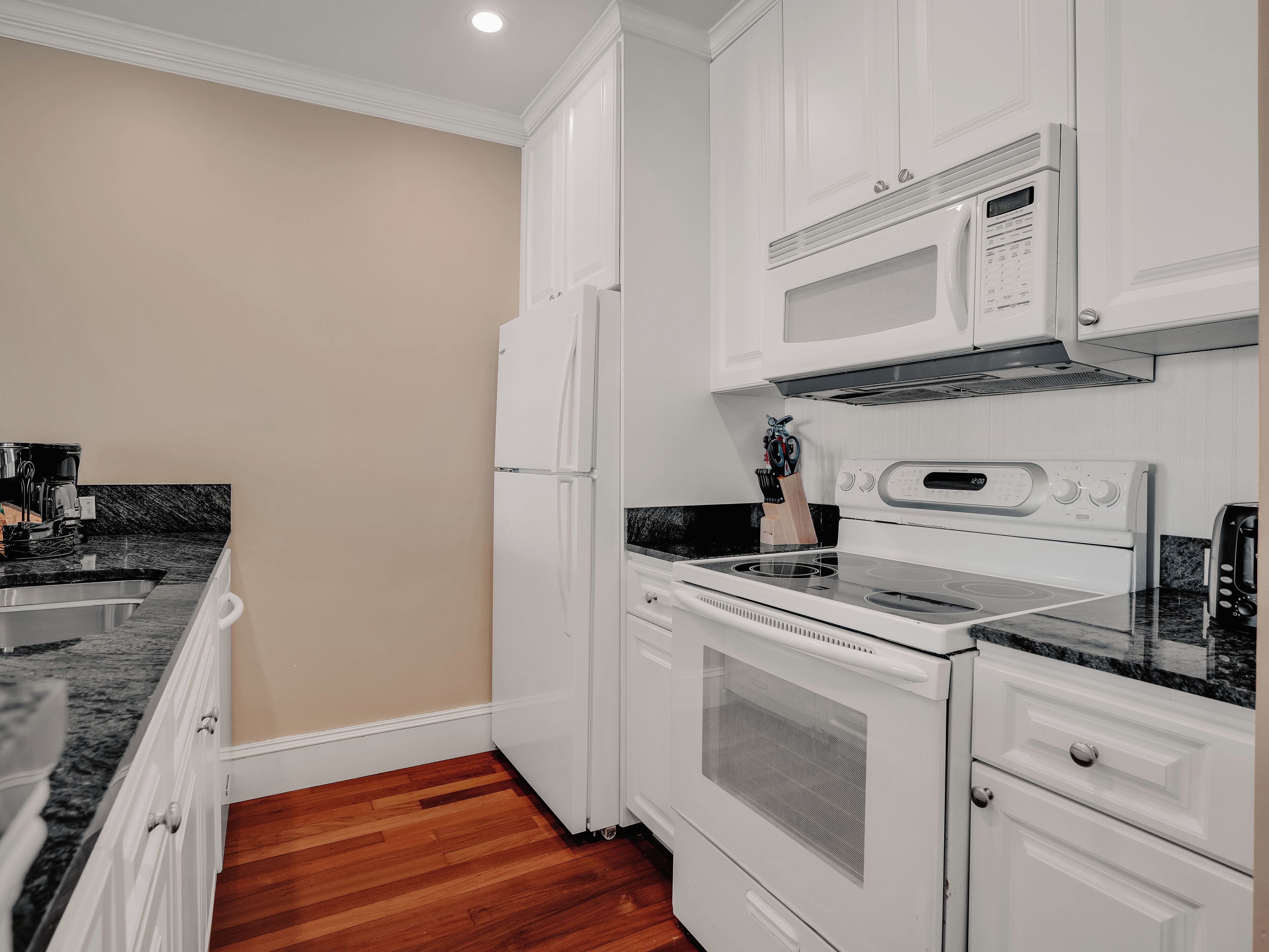 A compact kitchen with white cabinetry, a built-in microwave, a stove, and a coffee maker.