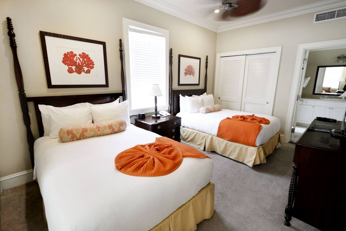 A hotel room with two beds, a nightstand, a dresser, and a large mirror.