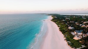 An aerial view of a beach with a pink sand shore, surrounded by lush greenery and houses. - Valentines Resort & Marina (Dunmore Town)