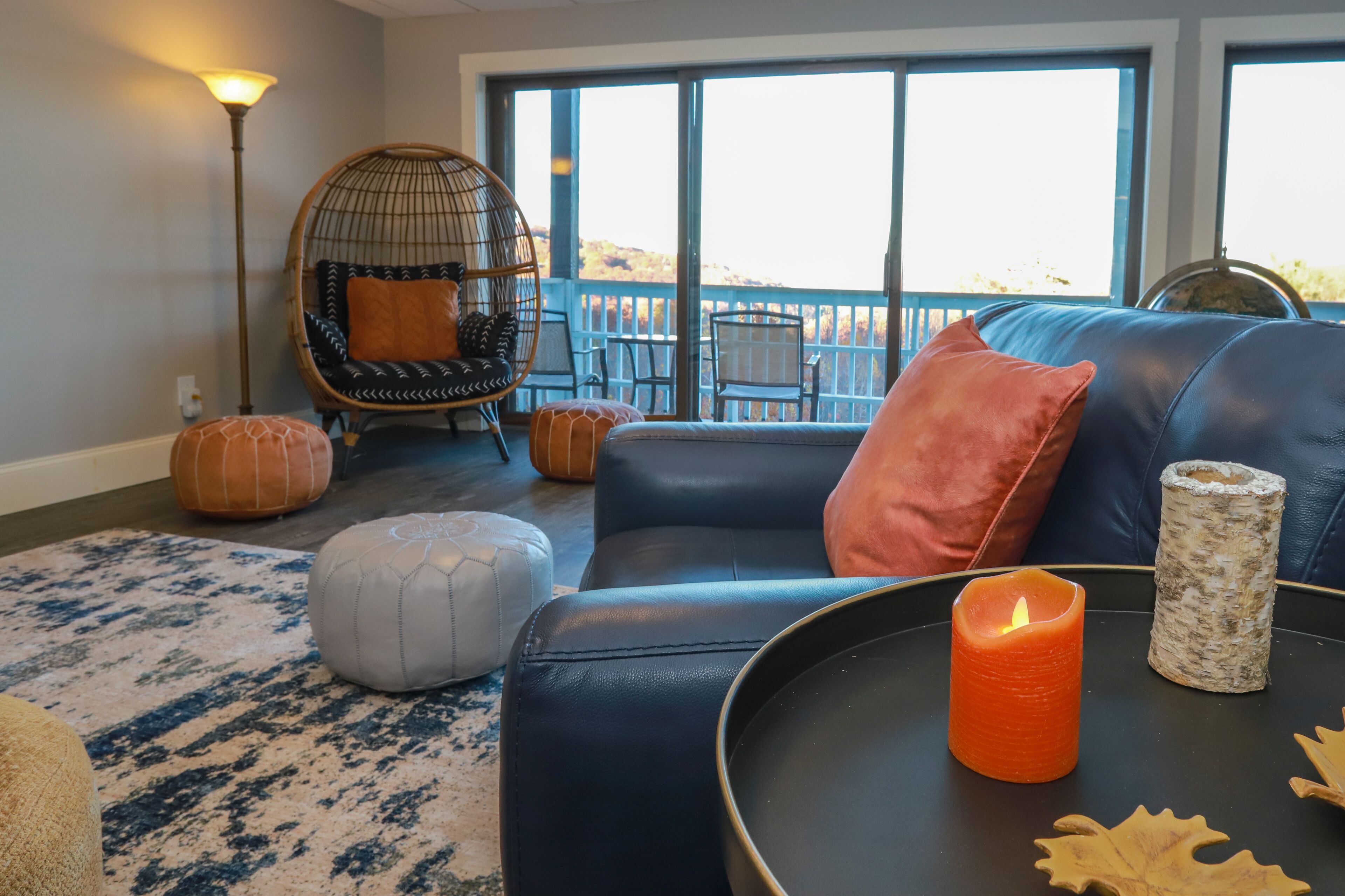 A cozy living room with a black leather sofa, a hanging chair, and a large window offering a view of the outdoors.