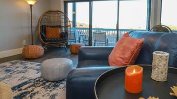 A cozy living room with a black leather sofa, a hanging chair, and a large window offering a view of the outdoors.