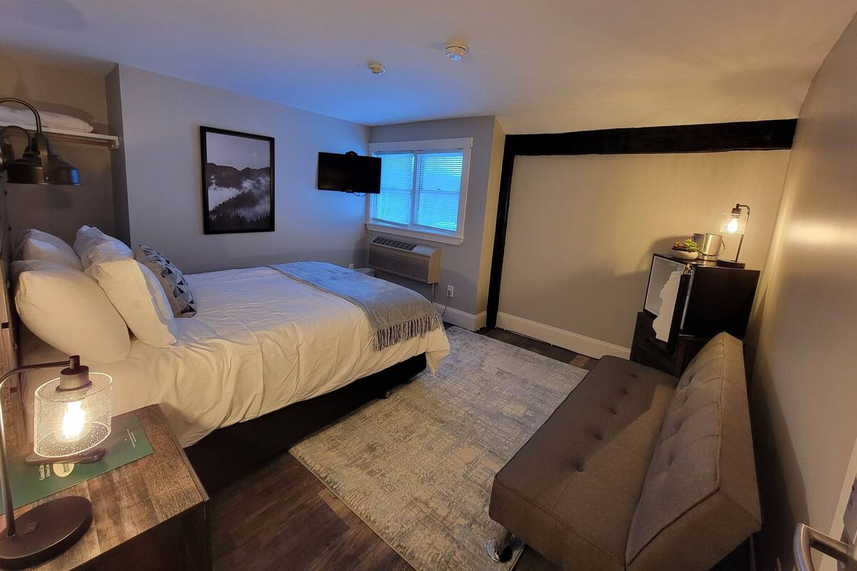 A bedroom with a bed, bedside table, lamp, and a TV mounted on the wall.