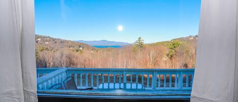 A view from a balcony with a railing, overlooking a landscape with trees and mountains in the distance.