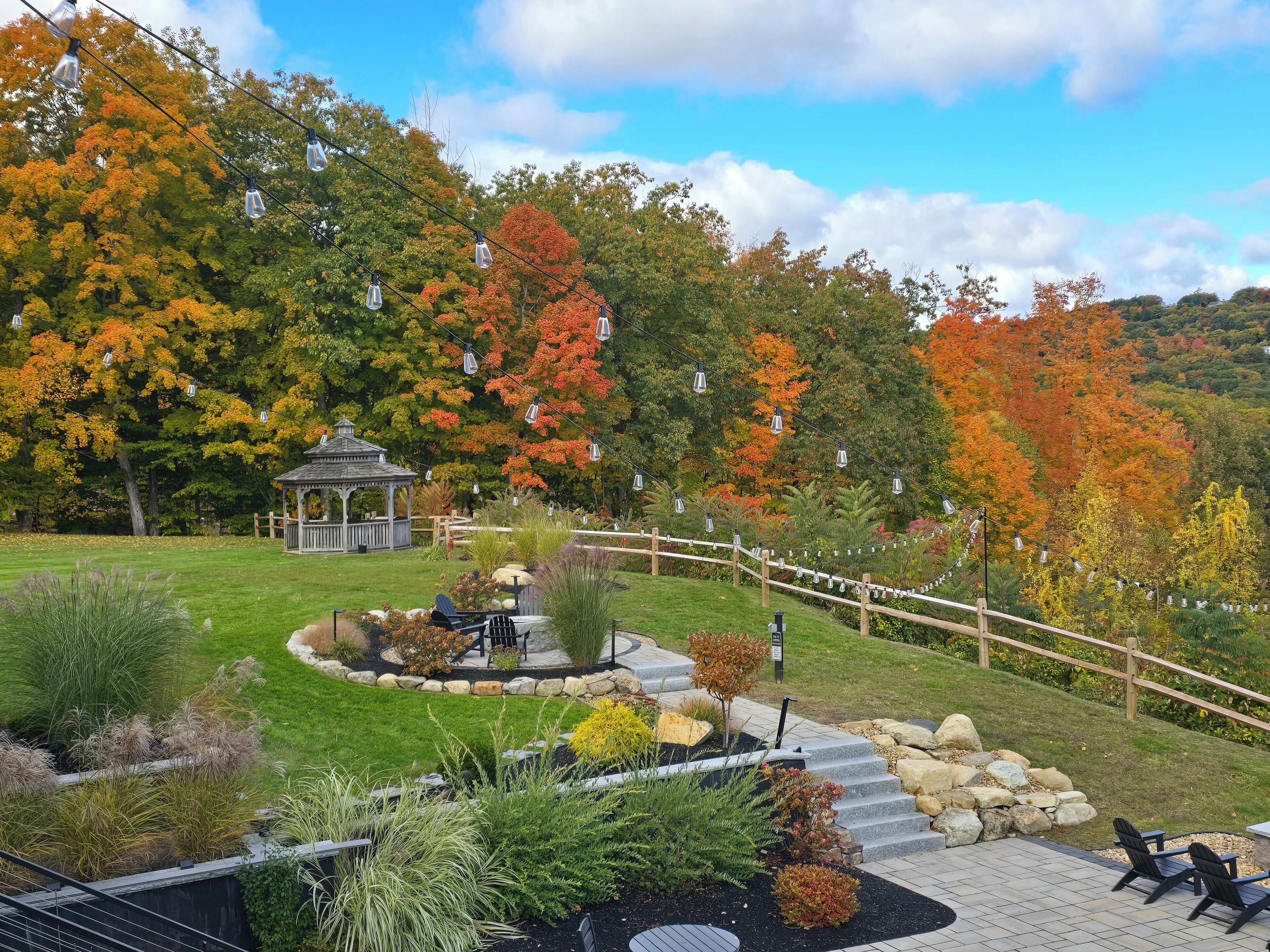 A gazebo in a landscaped garden with a wooden fence and steps leading up a hill.