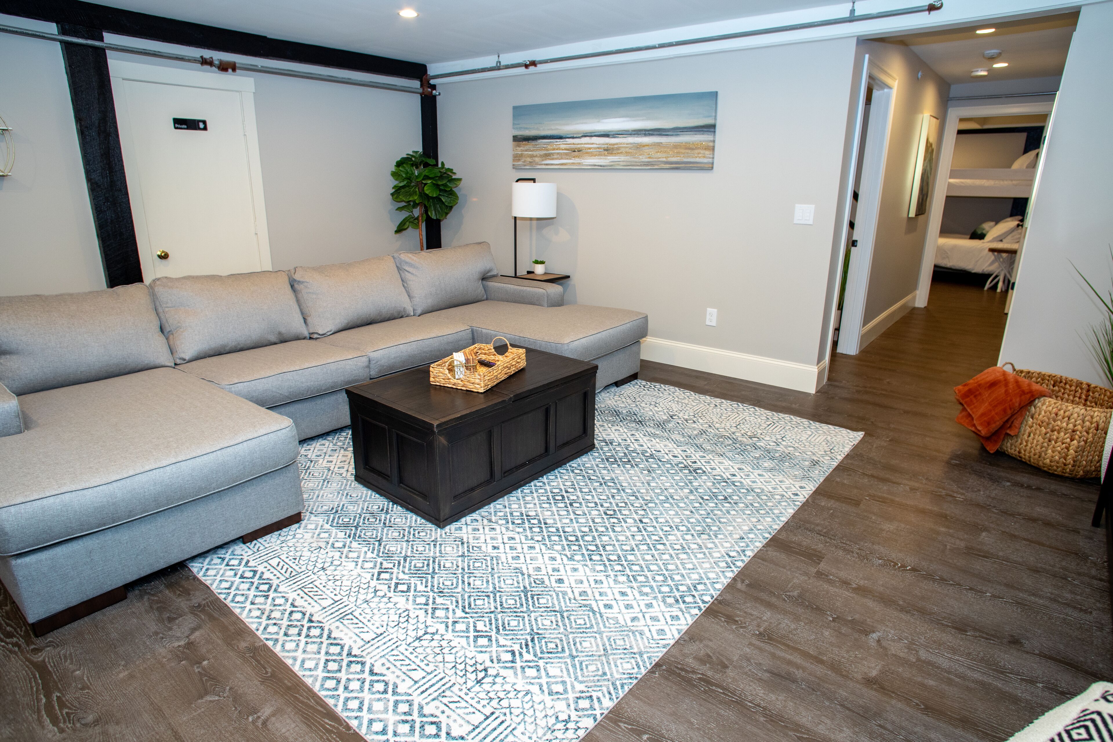 Un salon avec un canapé d’angle gris, une table basse en bois foncé et un tapis à motifs.