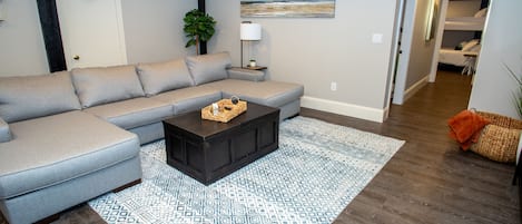 Un salon avec un canapé d’angle gris, une table basse en bois foncé et un tapis à motifs.