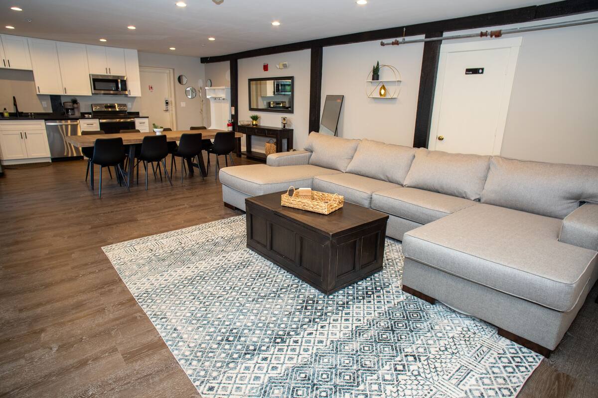 A modern living room with a sectional sofa, a coffee table, and a dining area with chairs and a table.