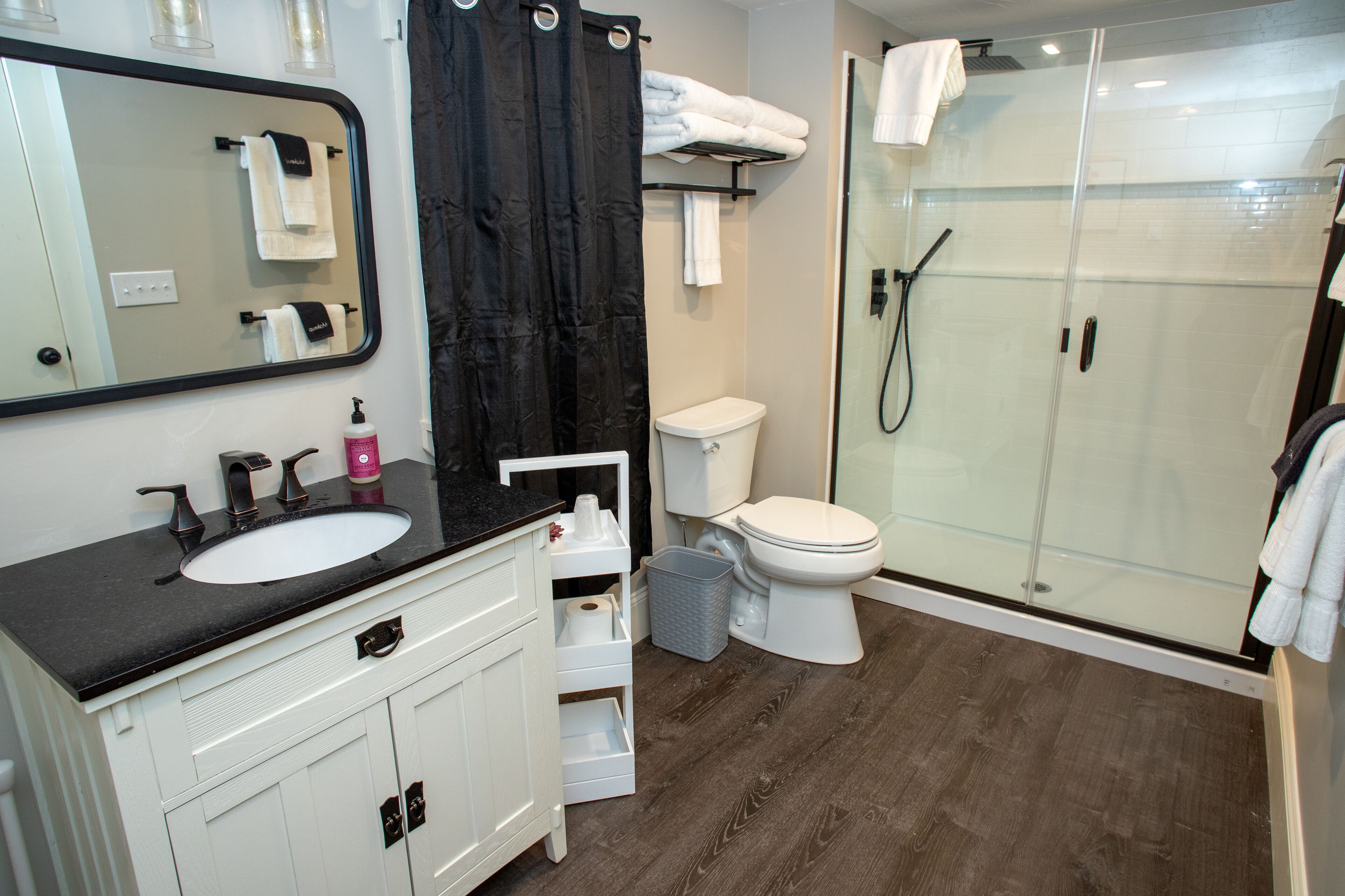 A modern bathroom with a black countertop sink, white cabinets, a glass shower enclosure, and a toilet.