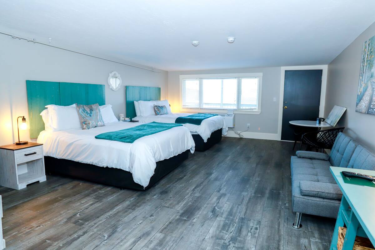 A modern hotel room with two beds, a sofa, a small table, and a desk.