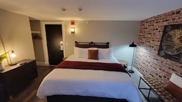 Et hotelværelse med en seng, et skrivebord, en lampe, en dør og en mur med et globus-kunstværk.