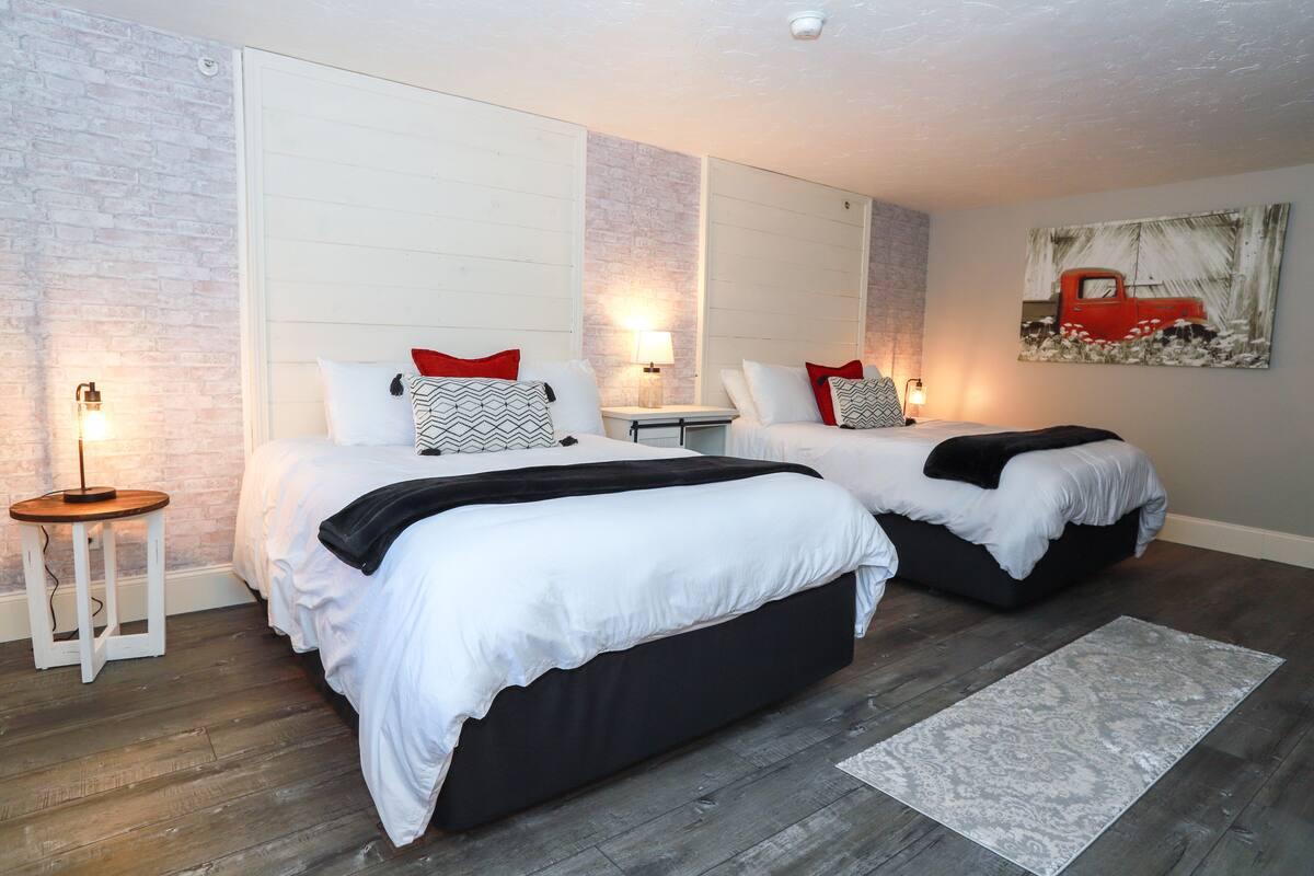 A bedroom with two beds, a nightstand, a lamp, and a painting on the wall.