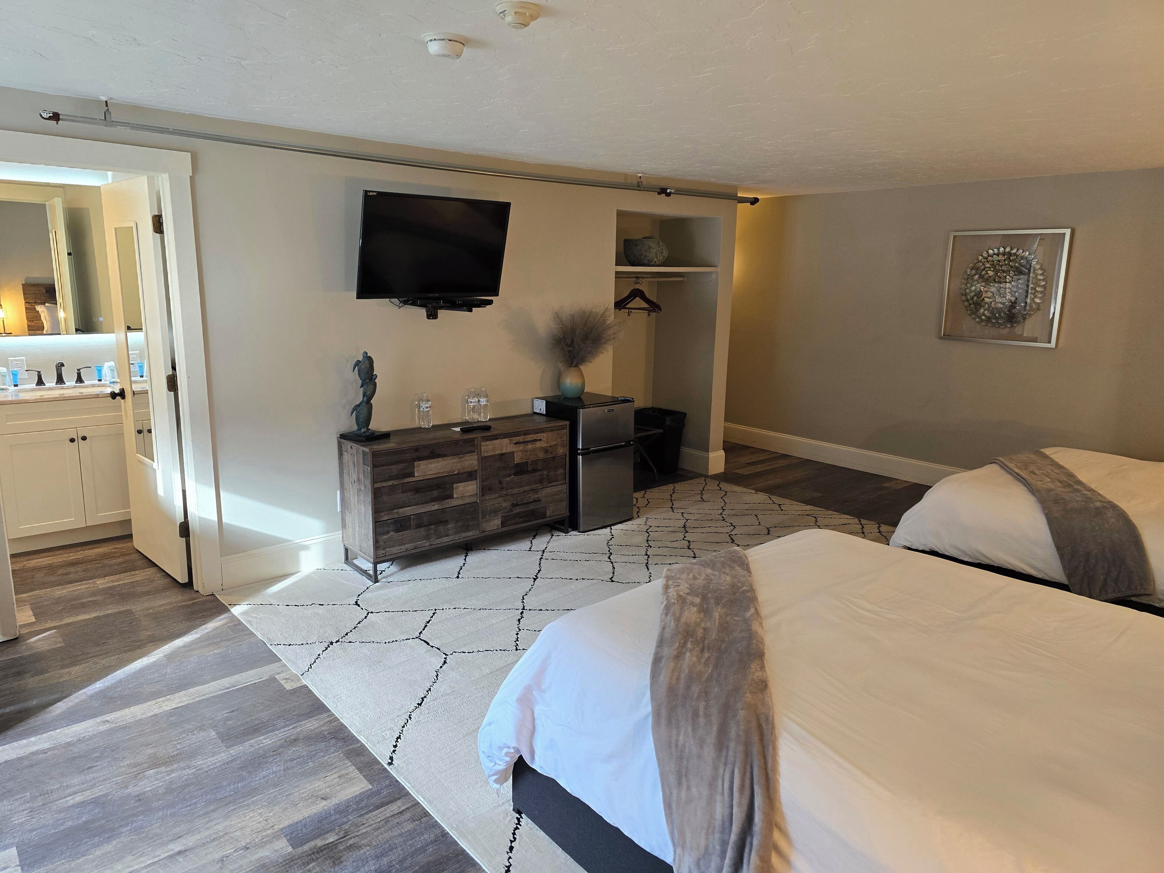 Quarto com duas camas, cômoda, televisão e banheiro visível por uma porta aberta.