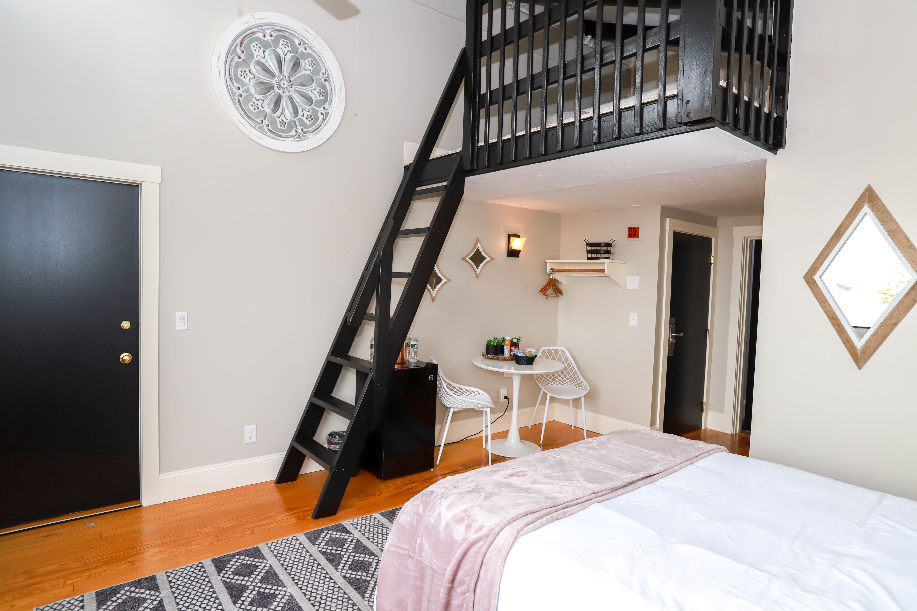 Une chambre à coucher avec un lit, un escalier noir, une petite table avec des chaises et un élément décoratif mural.